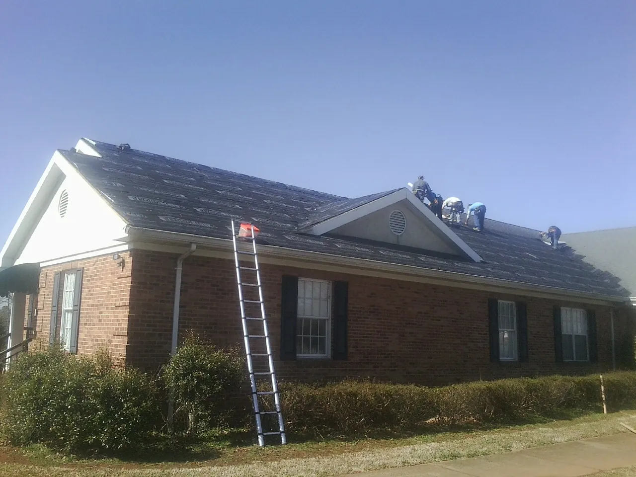 Crew tearing shingles off a brick ranch roof with a ladder set — Emergency Roof Repair work by our crew in Slatersville