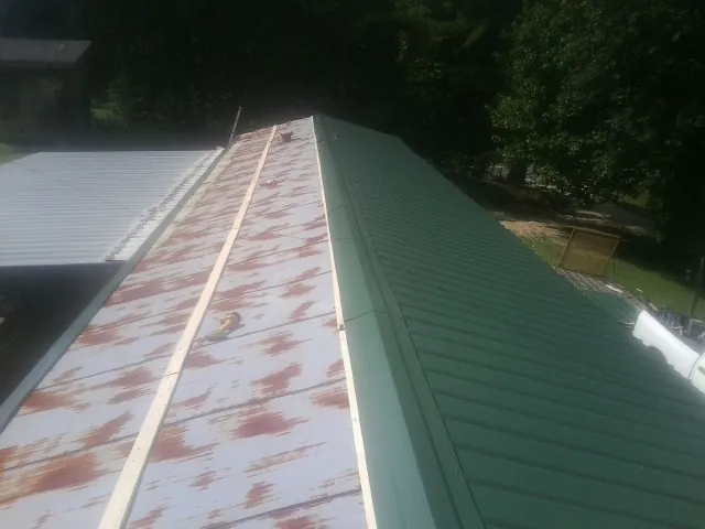 Old rusted panels beside newly installed green metal roofing — Wind Damage Roof Repair by Roofing Brothers in Slatersville