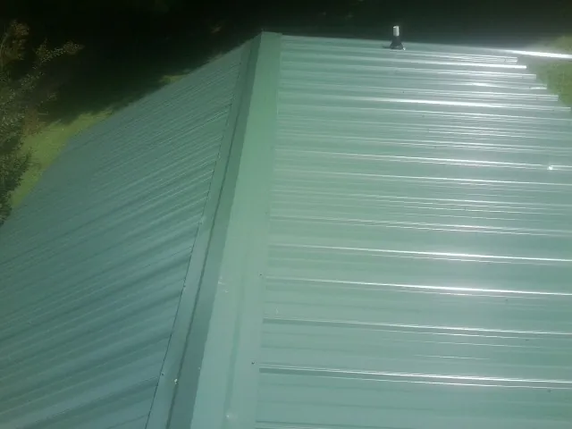 New green metal panels meeting at the ridge of a roof — Flat Roof Repair work by our crew in Slatersville