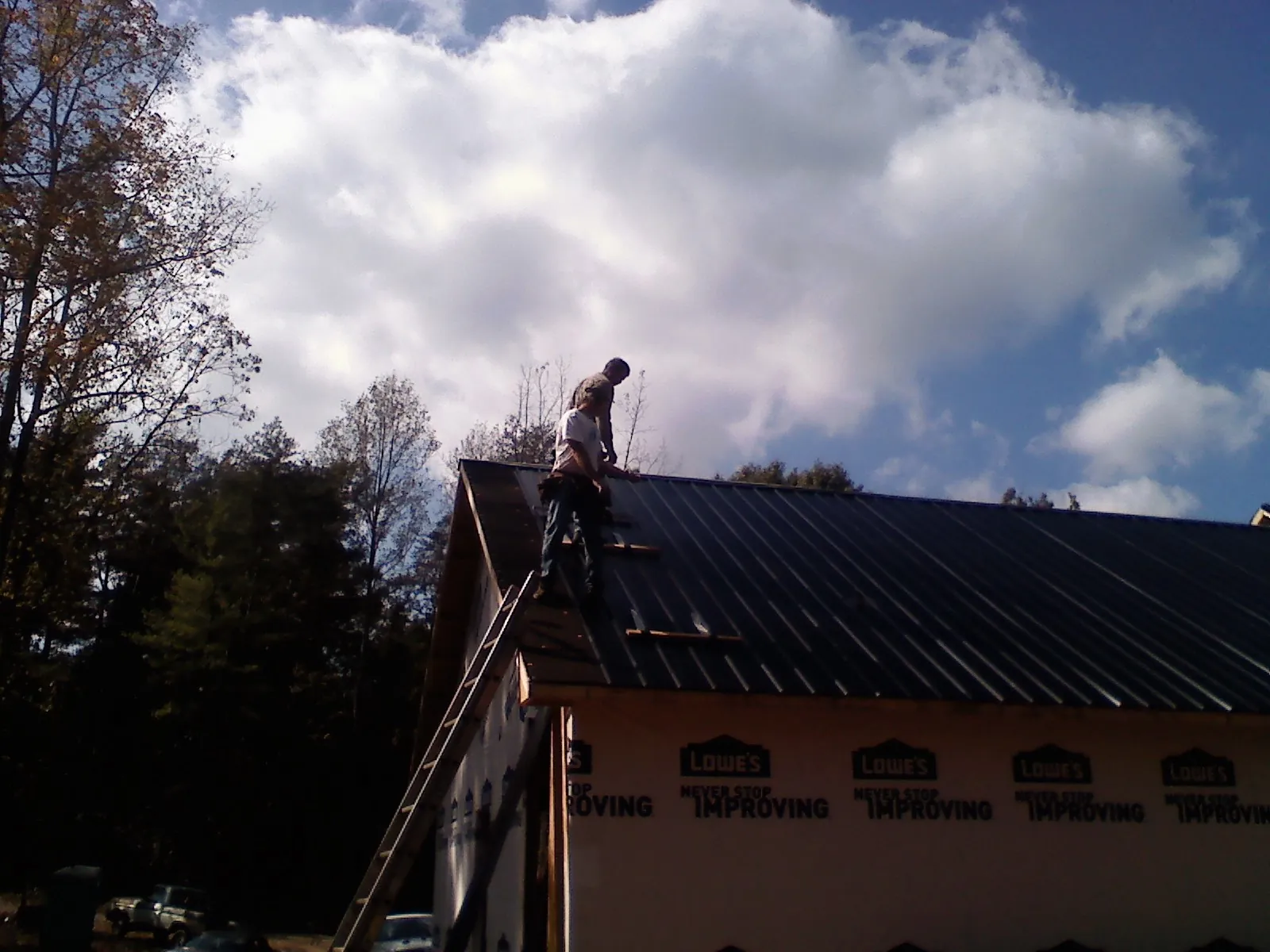 Roofer fastening dark metal panels high against a cloudy sky, from a Roof Inspection job in Slatersville