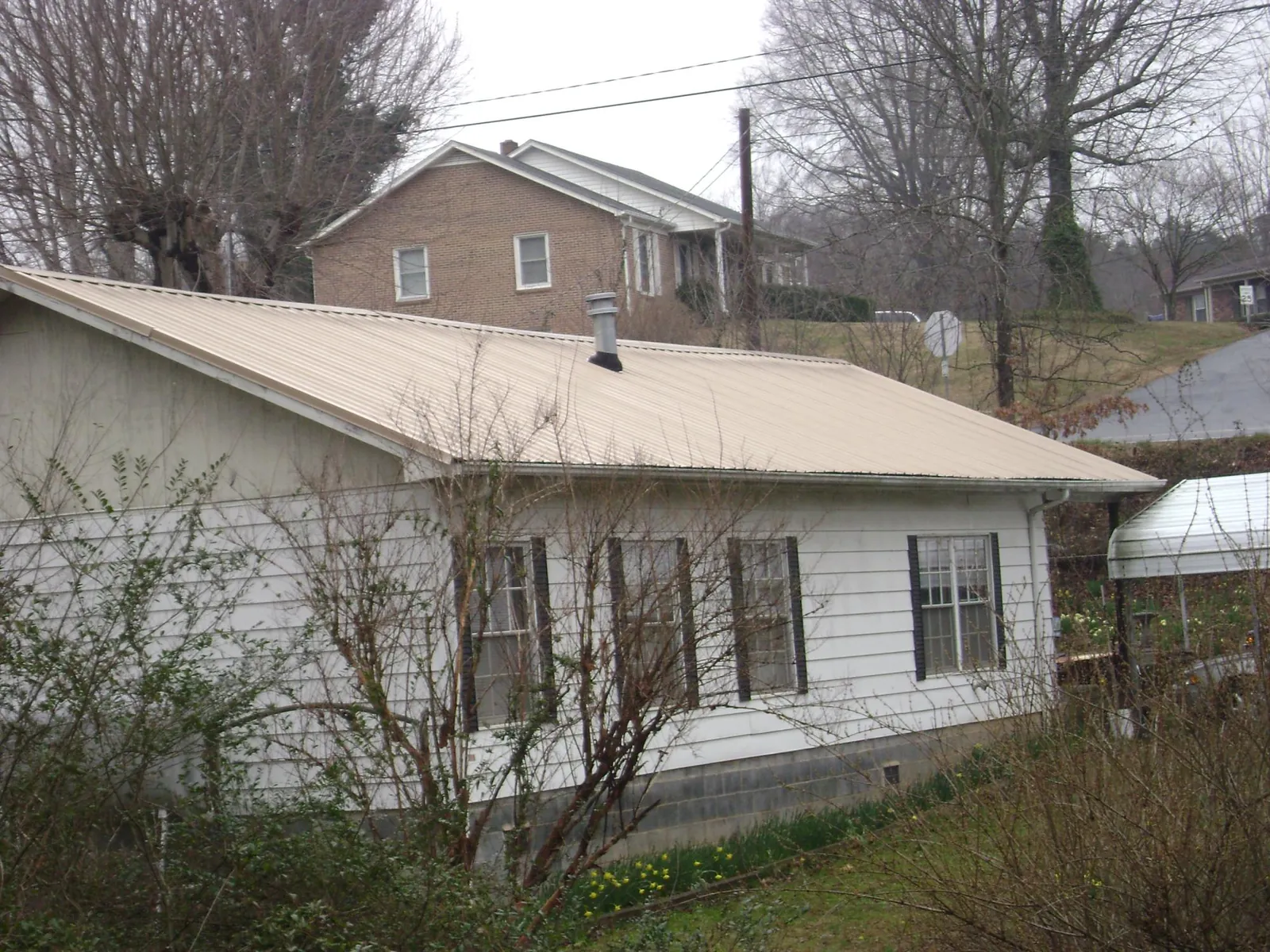 Tan metal roof on a white sided house set into a hillside — Commercial Roofing by Roofing Brothers in Slatersville