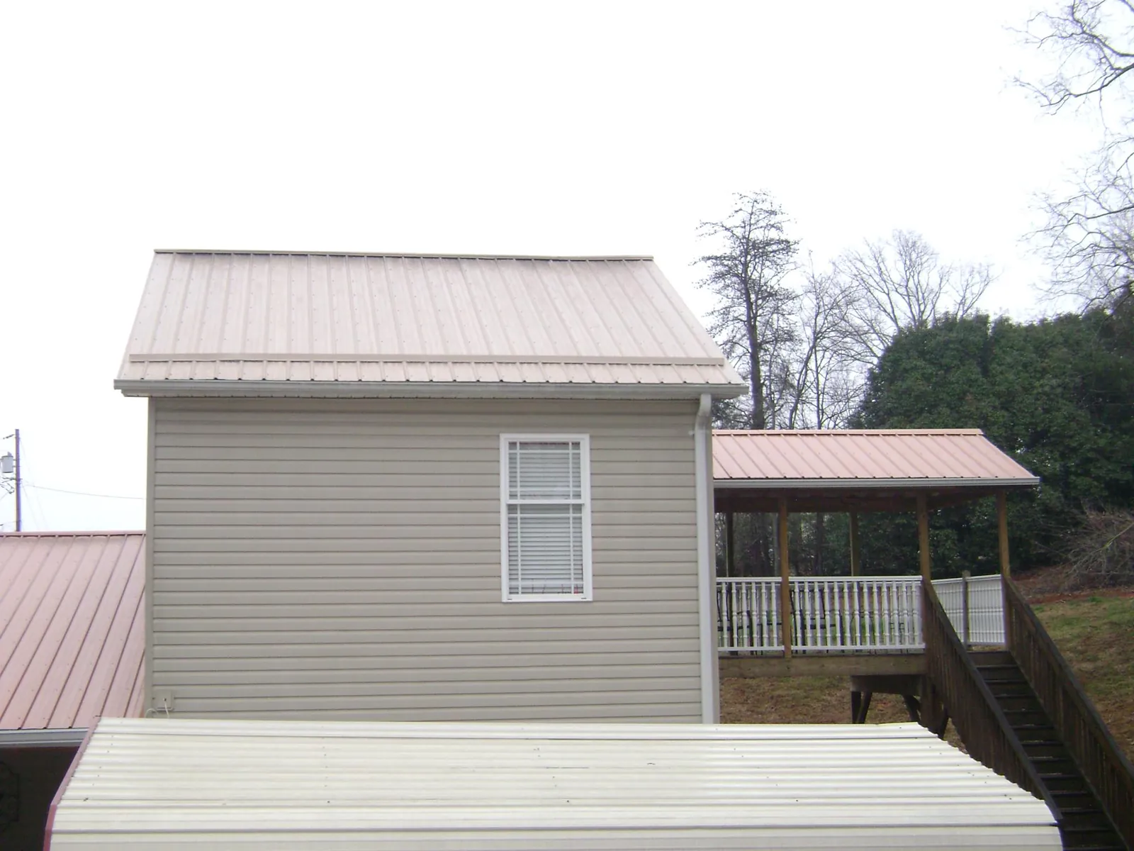 Tan metal roofs on a two story addition and attached porch, from a Roof Replacement job in Slatersville